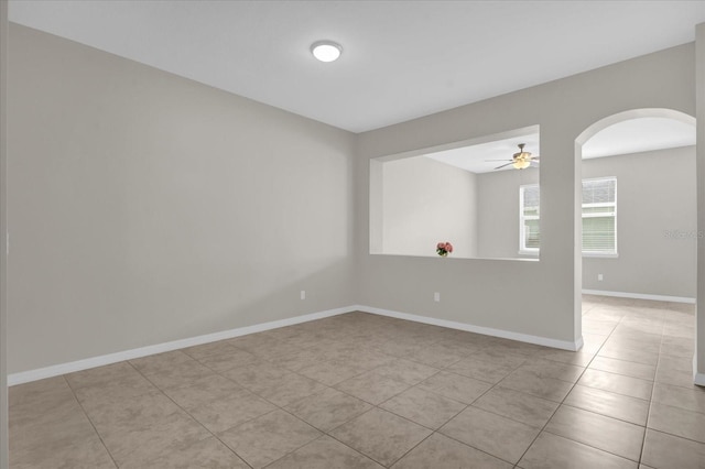 tiled empty room featuring baseboards, arched walkways, and ceiling fan