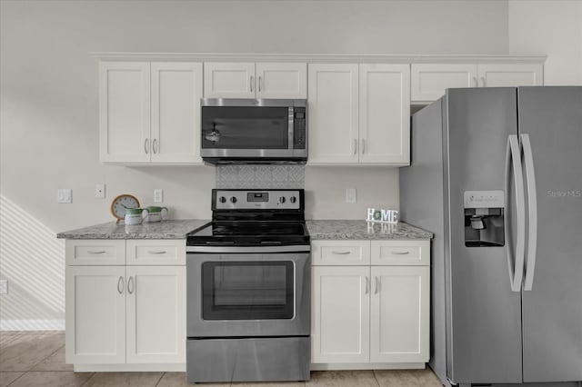 kitchen featuring appliances with stainless steel finishes, white cabinets, light stone counters, and light tile patterned floors