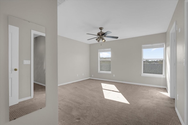 empty room with light colored carpet, a ceiling fan, and baseboards