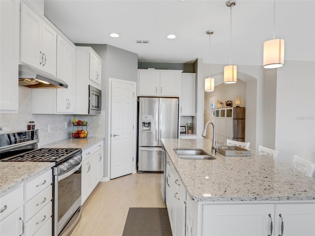 kitchen featuring appliances with stainless steel finishes, decorative light fixtures, white cabinetry, sink, and a center island with sink