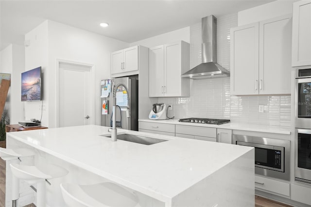 kitchen featuring a kitchen breakfast bar, appliances with stainless steel finishes, wall chimney exhaust hood, sink, and an island with sink