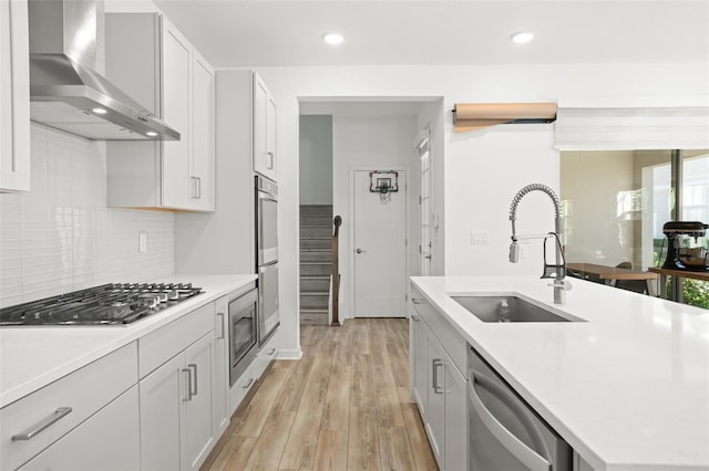 kitchen with white cabinets, wall chimney range hood, sink, and appliances with stainless steel finishes