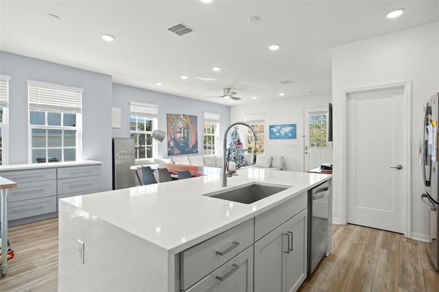 kitchen featuring gray cabinetry, dishwasher, a center island with sink, sink, and ceiling fan