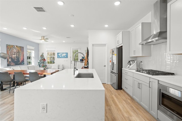 kitchen featuring a center island with sink, wall chimney exhaust hood, stainless steel appliances, and sink