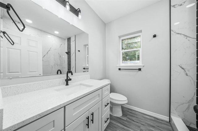 bathroom featuring a tile shower, vanity, hardwood / wood-style flooring, and toilet