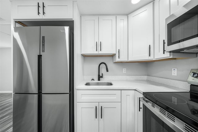 kitchen with appliances with stainless steel finishes, light stone counters, sink, white cabinets, and hardwood / wood-style floors