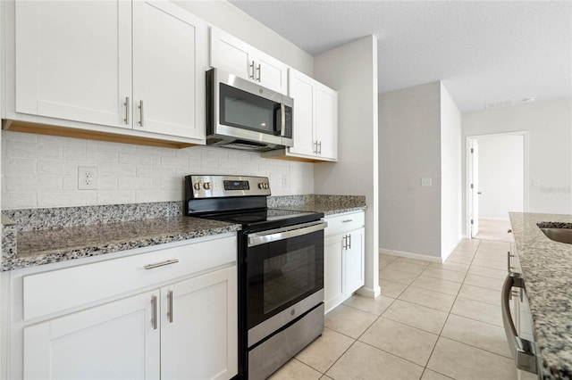 kitchen featuring light stone countertops, appliances with stainless steel finishes, a textured ceiling, white cabinets, and light tile patterned flooring