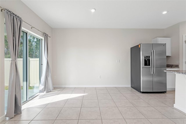 kitchen featuring white cabinets, stainless steel fridge, light stone countertops, and light tile patterned floors