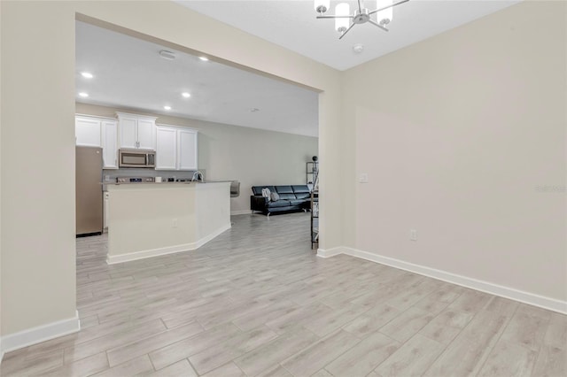 kitchen with an inviting chandelier, white cabinetry, appliances with stainless steel finishes, and light hardwood / wood-style flooring