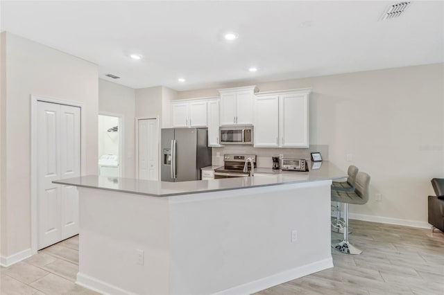 kitchen featuring kitchen peninsula, appliances with stainless steel finishes, a kitchen bar, and white cabinetry