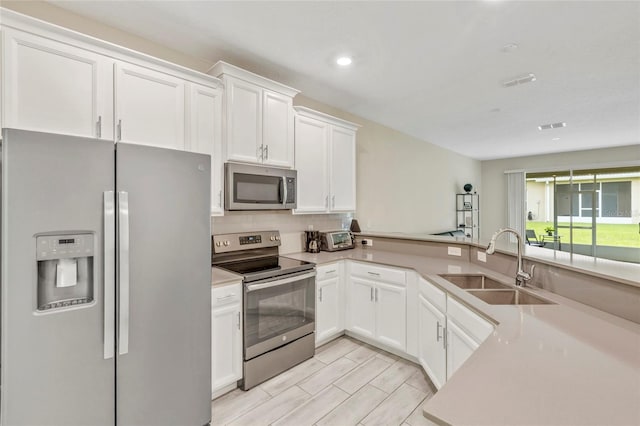 kitchen featuring kitchen peninsula, white cabinetry, sink, and appliances with stainless steel finishes