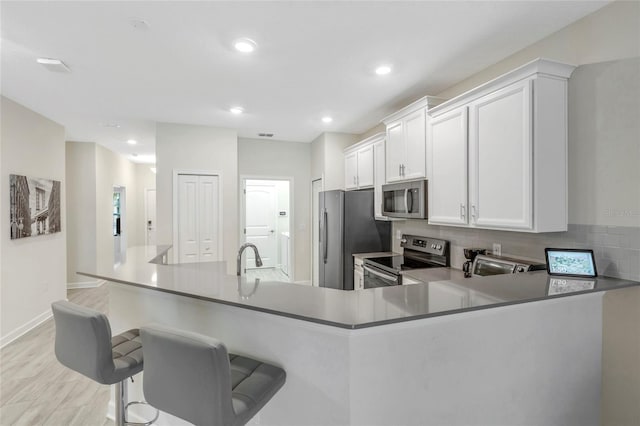 kitchen with kitchen peninsula, tasteful backsplash, stainless steel appliances, white cabinetry, and a breakfast bar area