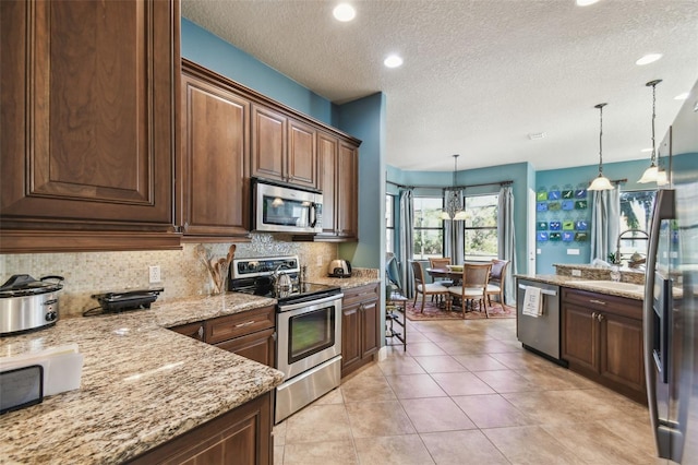 kitchen featuring hanging light fixtures, light stone counters, a textured ceiling, decorative backsplash, and appliances with stainless steel finishes