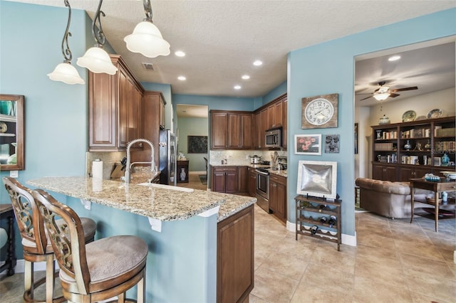 kitchen featuring kitchen peninsula, backsplash, stainless steel appliances, ceiling fan, and decorative light fixtures