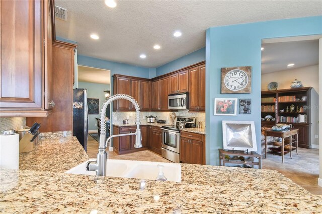 kitchen with decorative backsplash, kitchen peninsula, light stone countertops, stainless steel appliances, and sink