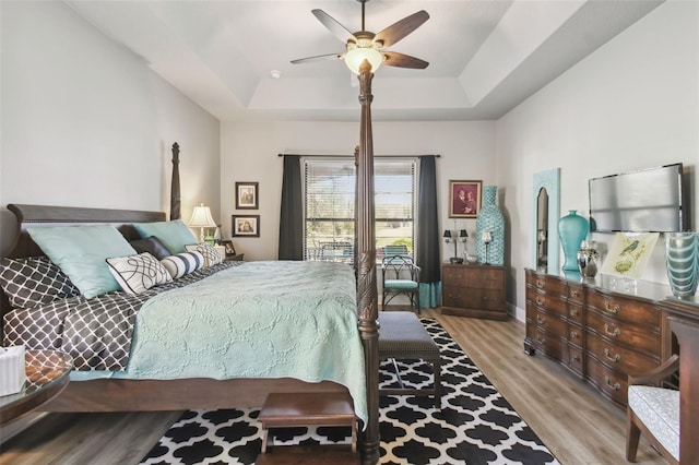 bedroom with ceiling fan, a raised ceiling, and light wood-type flooring