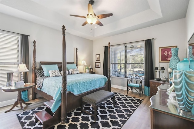 bedroom featuring hardwood / wood-style floors, ceiling fan, a raised ceiling, and multiple windows