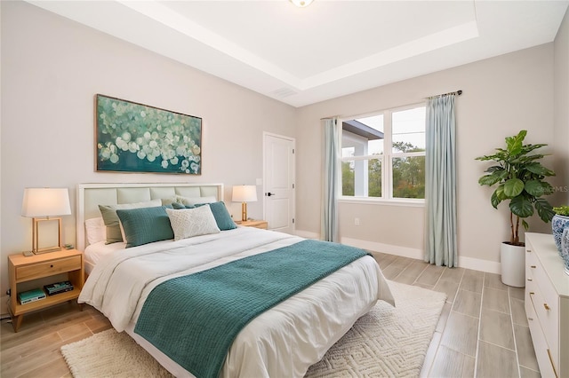 bedroom featuring wood tiled floor, baseboards, and a raised ceiling