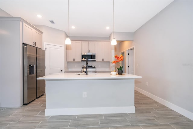 kitchen featuring stainless steel appliances, light countertops, hanging light fixtures, and a center island with sink