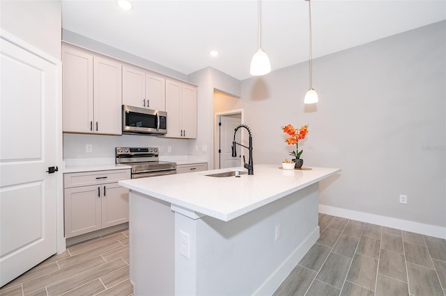 kitchen featuring pendant lighting, stainless steel appliances, light countertops, a sink, and an island with sink