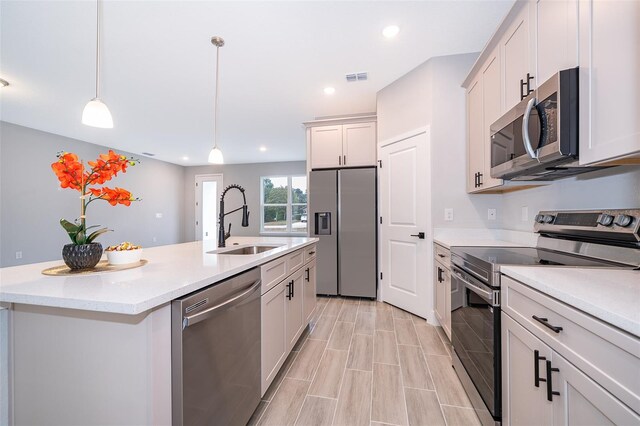 kitchen featuring a center island with sink, stainless steel appliances, hanging light fixtures, white cabinetry, and a sink