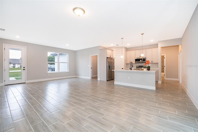 interior space with open floor plan, hanging light fixtures, a kitchen island with sink, stainless steel appliances, and light countertops