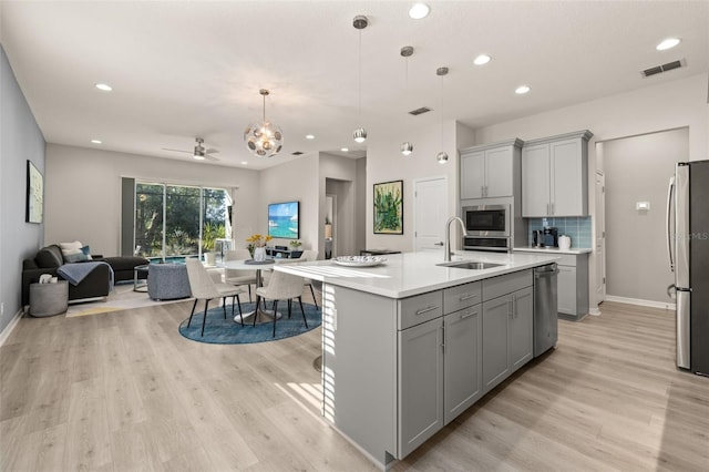 kitchen featuring gray cabinets, ceiling fan, an island with sink, and stainless steel appliances