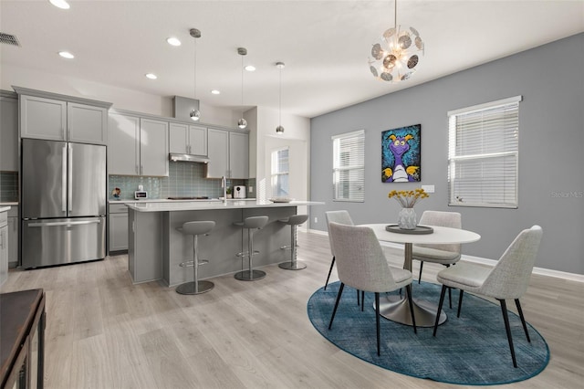 kitchen with pendant lighting, a center island with sink, stainless steel refrigerator, and gray cabinetry