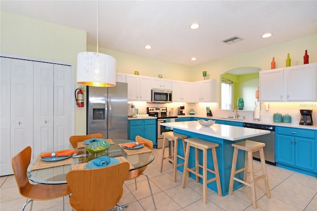 kitchen featuring stainless steel appliances, blue cabinetry, white cabinets, a kitchen island, and hanging light fixtures