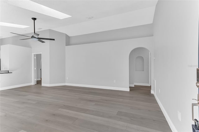 unfurnished living room with wood-type flooring, ceiling fan, and vaulted ceiling with skylight