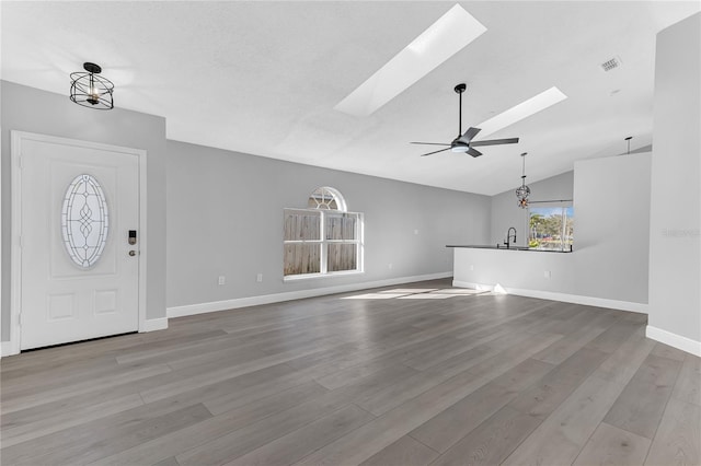 entrance foyer featuring ceiling fan with notable chandelier, sink, light hardwood / wood-style flooring, and vaulted ceiling with skylight