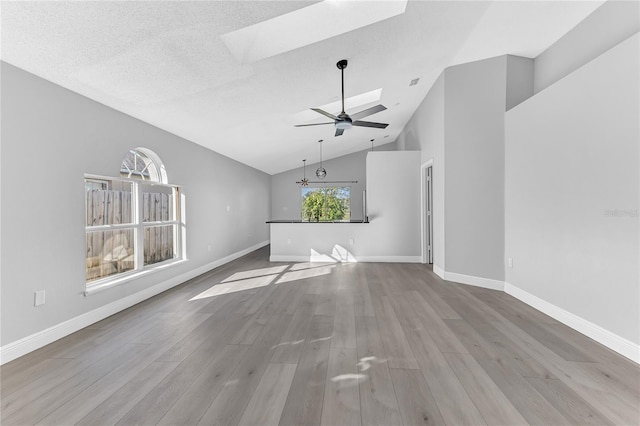 unfurnished living room featuring ceiling fan with notable chandelier, a textured ceiling, light wood-type flooring, and vaulted ceiling with skylight