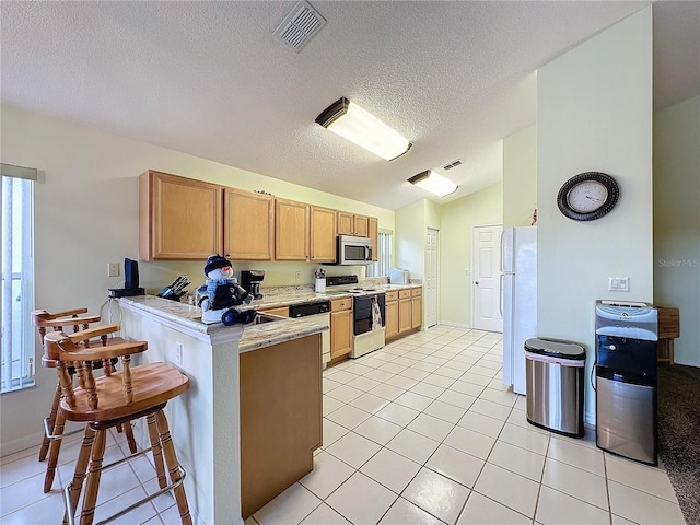 kitchen featuring white appliances, light tile patterned floors, a textured ceiling, kitchen peninsula, and a breakfast bar area