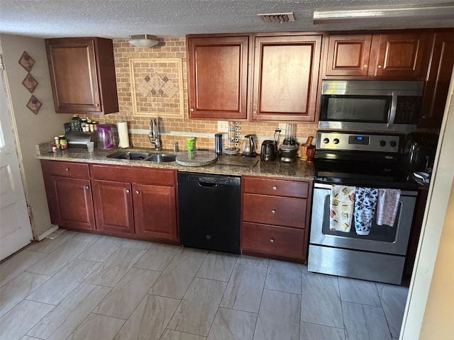 kitchen with a textured ceiling, stainless steel appliances, dark stone counters, and sink