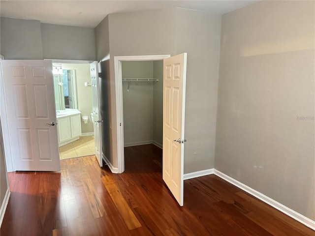 unfurnished bedroom featuring hardwood / wood-style floors, ensuite bath, a walk in closet, and a closet