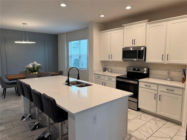 kitchen with stainless steel appliances, white cabinetry, an island with sink, and sink