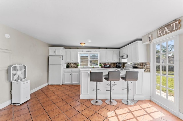 kitchen with tasteful backsplash, light tile patterned flooring, white appliances, a breakfast bar, and white cabinets