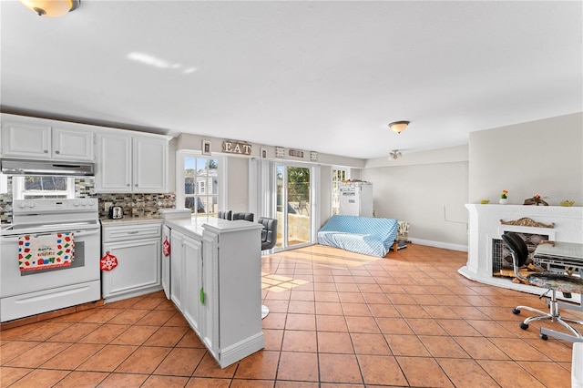 kitchen with kitchen peninsula, backsplash, electric range, white cabinets, and light tile patterned flooring