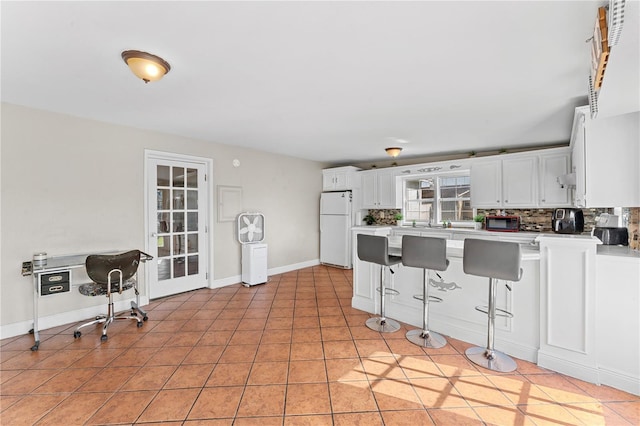 kitchen with a breakfast bar, light tile patterned flooring, tasteful backsplash, white fridge, and white cabinetry