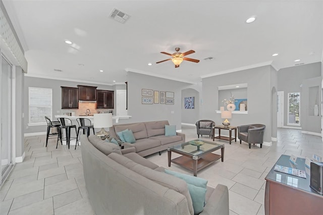 tiled living room with ceiling fan, sink, and crown molding