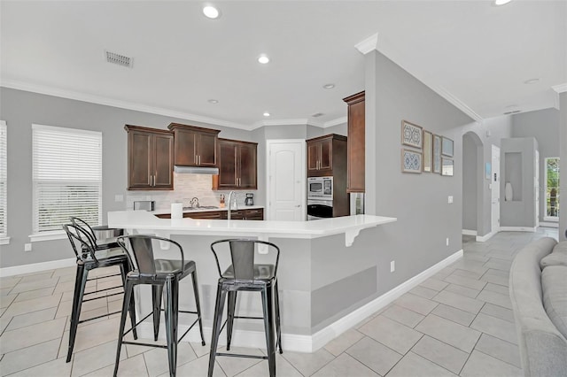 kitchen featuring appliances with stainless steel finishes, a kitchen bar, ornamental molding, kitchen peninsula, and light tile patterned flooring