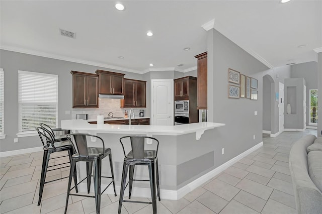 kitchen with light tile patterned floors, appliances with stainless steel finishes, ornamental molding, a kitchen bar, and kitchen peninsula