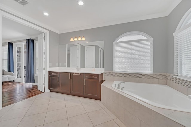 bathroom featuring crown molding, plenty of natural light, vanity, tiled tub, and tile patterned flooring