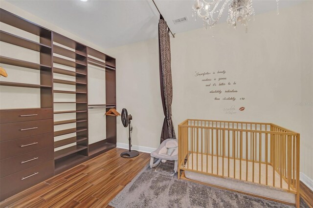 bedroom featuring a nursery area, an inviting chandelier, and hardwood / wood-style floors