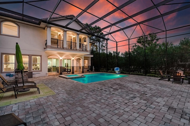 pool at dusk featuring a fire pit, an in ground hot tub, a lanai, and a patio area