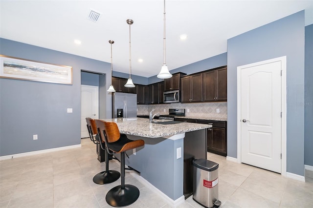 kitchen with light stone countertops, stainless steel appliances, pendant lighting, decorative backsplash, and a center island with sink