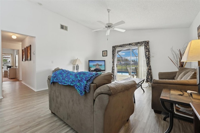 living room featuring a textured ceiling, ceiling fan, light hardwood / wood-style floors, and lofted ceiling