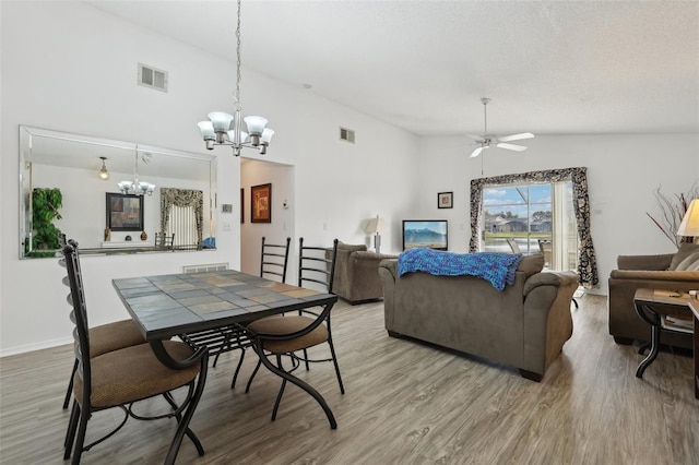 dining space with wood-type flooring, ceiling fan with notable chandelier, a textured ceiling, and lofted ceiling