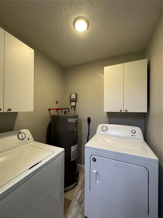 washroom with washing machine and clothes dryer, light wood-type flooring, water heater, a textured ceiling, and cabinets