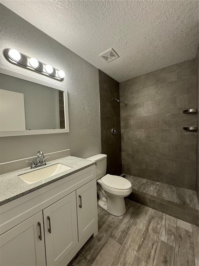 bathroom with toilet, a textured ceiling, a tile shower, and vanity